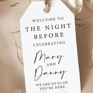 May include: A white rectangular paper tag with a jute twine loop at the top. The text reads: WELCOME TO THE NIGHT BEFORE CELEBRATING Mary AND Danny WE ARE SO GLAD YOU'RE HERE. The bottom of the tag features the text Recipe Box Designs.