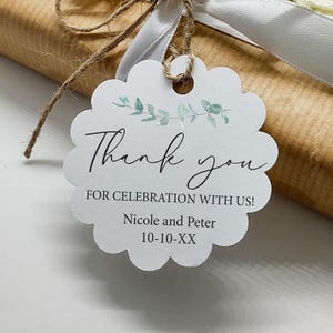 May include: A gift wrapped in brown paper, tied with white ribbon and twine, and adorned with a white flower. A scalloped tag reads "Thank you" with the names Nicole and Peter and a date.