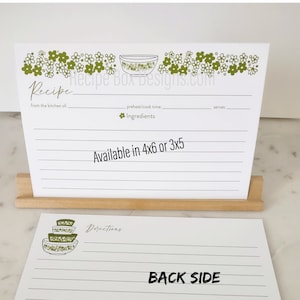 May include: A white recipe card with a green floral border and a green bowl design. The card has lines for writing down a recipe, including ingredients, directions, and serving size. The text "Recipe Box Designs.com" is printed on the card. The card is available in two sizes: 4x6 or 3x5 inches.
