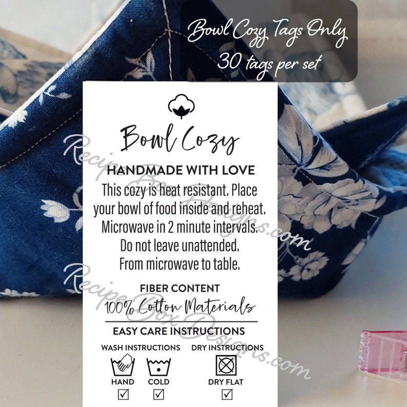 May include: A white tag with black text that reads "Bowl Cozy Handmade with Love". The tag also includes instructions for using the cozy, such as "This cozy is heat resistant. Place your bowl of food inside and reheat. Microwave in 2 minute intervals. Do not leave unattended. From microwave to table." The tag also includes the fiber content, which is 100% cotton, and easy care instructions, which include hand washing, cold washing, and drying flat.