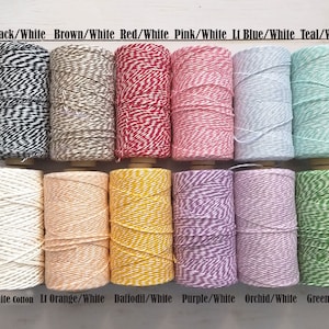 May include: A collection of twine spools in various colors, including black/white, brown/white, red/white, pink/white, light blue/white, and teal/white. Additional colors are very white cotton, light orange/white, daffodil/white, purple/white, orchid/white, and green/white. Each spool is labeled with its color combination.