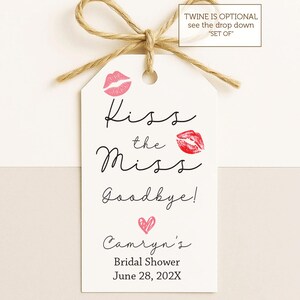May include: A white tag with the text "Kiss the Miss Goodbye!" and "Camryn's Bridal Shower June 28, 202X". The tag features pink lip prints and a heart, with a twine bow at the top.