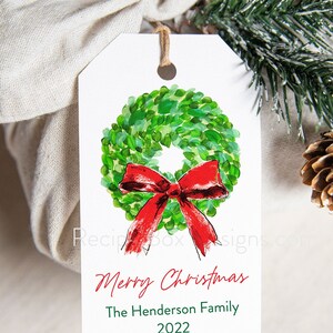 May include: A white gift tag with a watercolor wreath and red bow. The tag reads "Merry Christmas" and "The Henderson Family 2022". A twine string is attached to the tag.