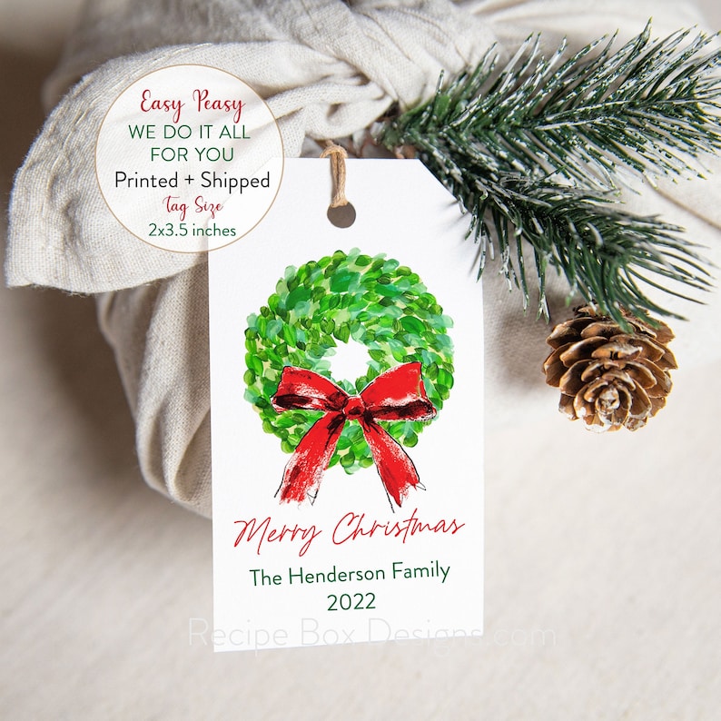 May include: A white gift tag with a watercolor wreath and red bow design. The tag reads "Merry Christmas" and includes a family name and the year 2022. Tag size is 2x3.5 inches.