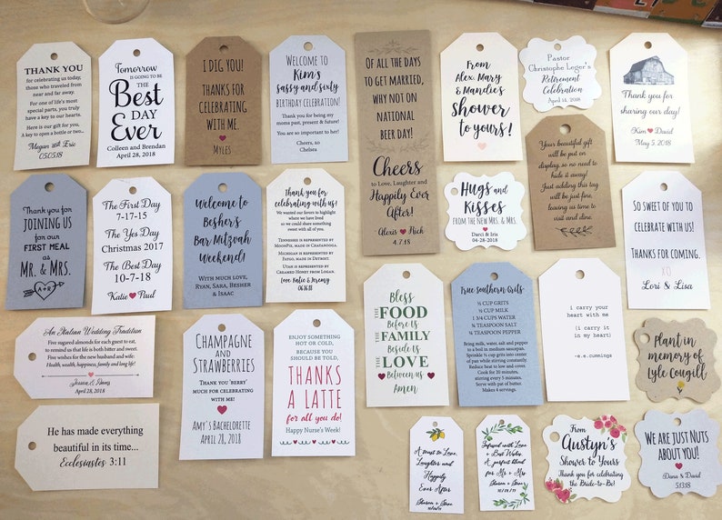 May include: A collection of various gift tags with handwritten text in black ink. The tags are in different shapes and sizes, with messages for weddings, birthdays, and other celebrations. Some tags have decorative elements like hearts and floral designs.