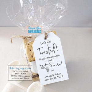 May include: A clear cellophane bag tied with twine, containing a s'mores kit. A white tag with the text "Let's Get Toasted!" hangs from the twine. The tag also includes the text "Roast a Marshmallow and Party S'more!" and the names Ashley & Robert.