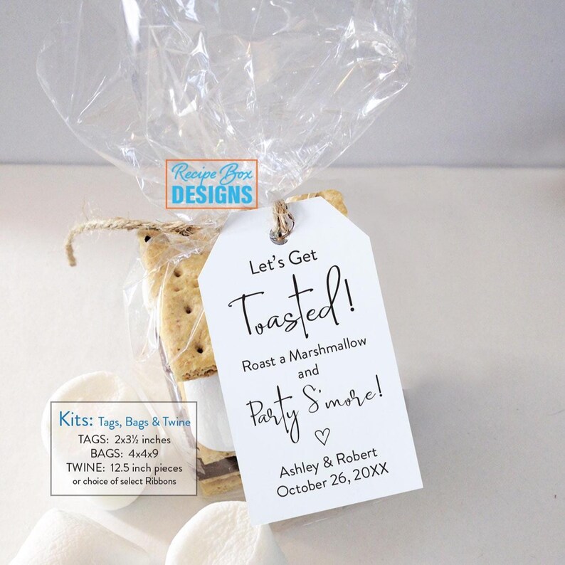 May include: A clear cellophane bag tied with twine, containing a s'mores kit. A white tag with the text "Let's Get Toasted!" hangs from the twine. The tag also includes the text "Roast a Marshmallow and Party S'more!" and the names Ashley & Robert.