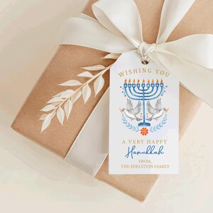 May include: A gift box wrapped in brown paper with a white ribbon and a decorative tag. The tag features a blue menorah, doves, and the text "Wishing You A Very Happy Hanukkah".