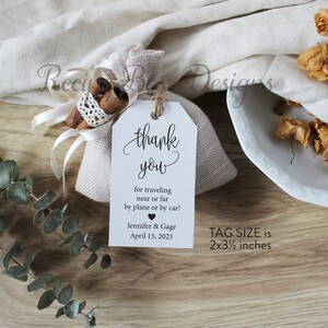 May include: A white tag with black text that says "thank you" for traveling near or far by plane or by car! Jennifer & Gage April 15, 2023. The tag is attached to a small burlap bag with cinnamon sticks and a white ribbon. The tag size is 2x3 1/2 inches.