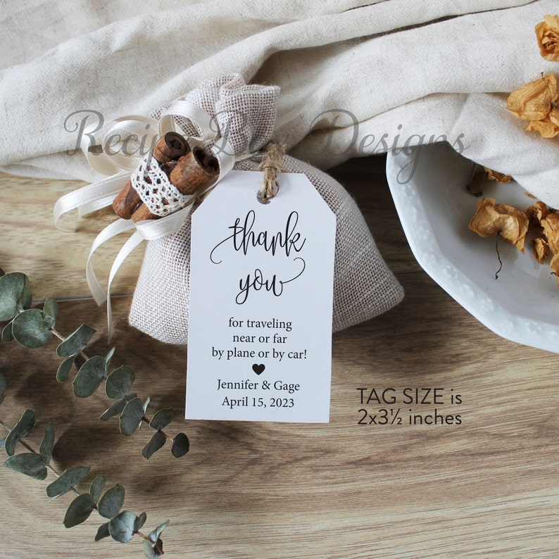 May include: A white tag with black text that says "thank you" for traveling near or far by plane or by car! Jennifer & Gage April 15, 2023. The tag is attached to a small burlap bag with cinnamon sticks and a white ribbon. The tag size is 2x3 1/2 inches.