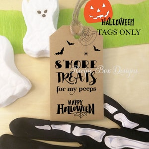 May include: A brown paper tag with the text "S'more Treats for my peeps" and "Happy Halloween" with a spiderweb design. The tag is decorated with bats and a pumpkin. White ghost-shaped marshmallows and black skeleton gloves are also visible.