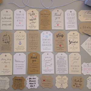 May include: Assortment of decorative tags with various messages for celebrations, including birthdays, weddings, and baby showers. The tags are in different shapes and sizes, with a variety of fonts and colors. A pair of scissors and twine are also present.