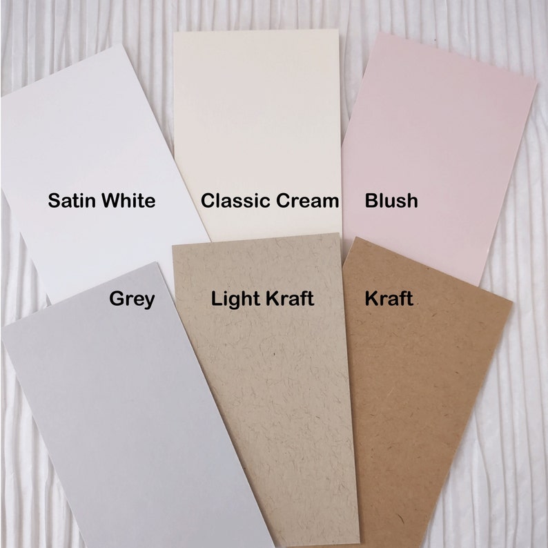 May include: A collection of rectangular paper samples in various colors, including satin white, classic cream, blush, grey, light kraft, and kraft. Each sample is labeled with its respective color name.