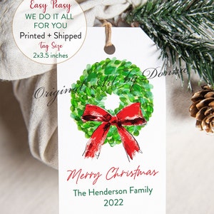 May include: A white Christmas gift tag with a watercolor wreath and red bow. The tag reads "Merry Christmas" and includes a family name and the year 2022. Tag size is 2x3.5 inches.