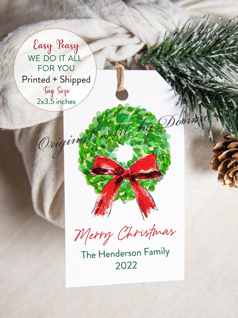 May include: A white Christmas gift tag with a watercolor wreath and red bow. The tag reads "Merry Christmas" and includes a family name and the year 2022. Tag size is 2x3.5 inches.