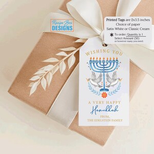 May include: A Hanukkah gift tag with a blue menorah, doves, and the text "Wishing You A Very Happy Hanukkah." The tag is tied to a wrapped gift with a white ribbon. The tag measures 2x3.5 inches.
