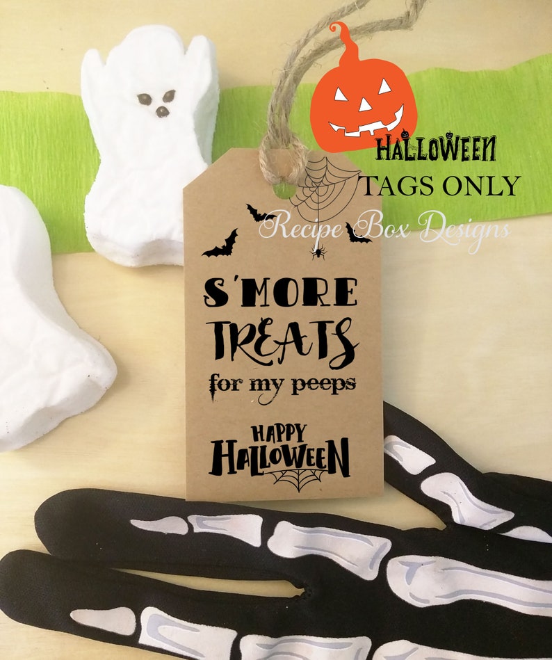 May include: A brown tag with the text "S'MORE TREATS for my peeps" and "Happy Halloween" with a spiderweb design. The tag is tied with twine and has a pumpkin and bats graphic. White ghost-shaped marshmallows and a skeleton hand are also in the image.