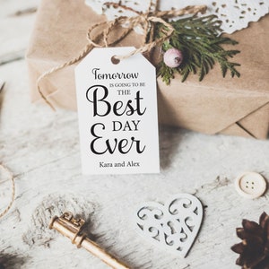 K&ouml;nnte beinhalten: Ein wei&szlig;es Geschenkanh&auml;nger mit schwarzem Text, der "Morgen wird der beste Tag aller Zeiten" lautet, mit den Namen Kara und Alex unten. Der Anh&auml;nger ist mit einer Schnur an einer braunen Geschenkbox gebunden.