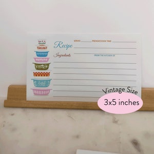 May include: A white recipe card with a stack of colorful vintage mixing bowls. The card has lines for writing down a recipe, including the title, ingredients, servings, preheat/cook time, and from the kitchen of. The card is 3x5 inches.