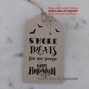 May include: A light kraft paper tag with a twine string. The tag features black text that reads "S'MORE TREATS for my peeps HAPPY HALLOWEEN." A spider web and bats are also printed on the tag. The text "Recipe Box Designs.com" is at the bottom.