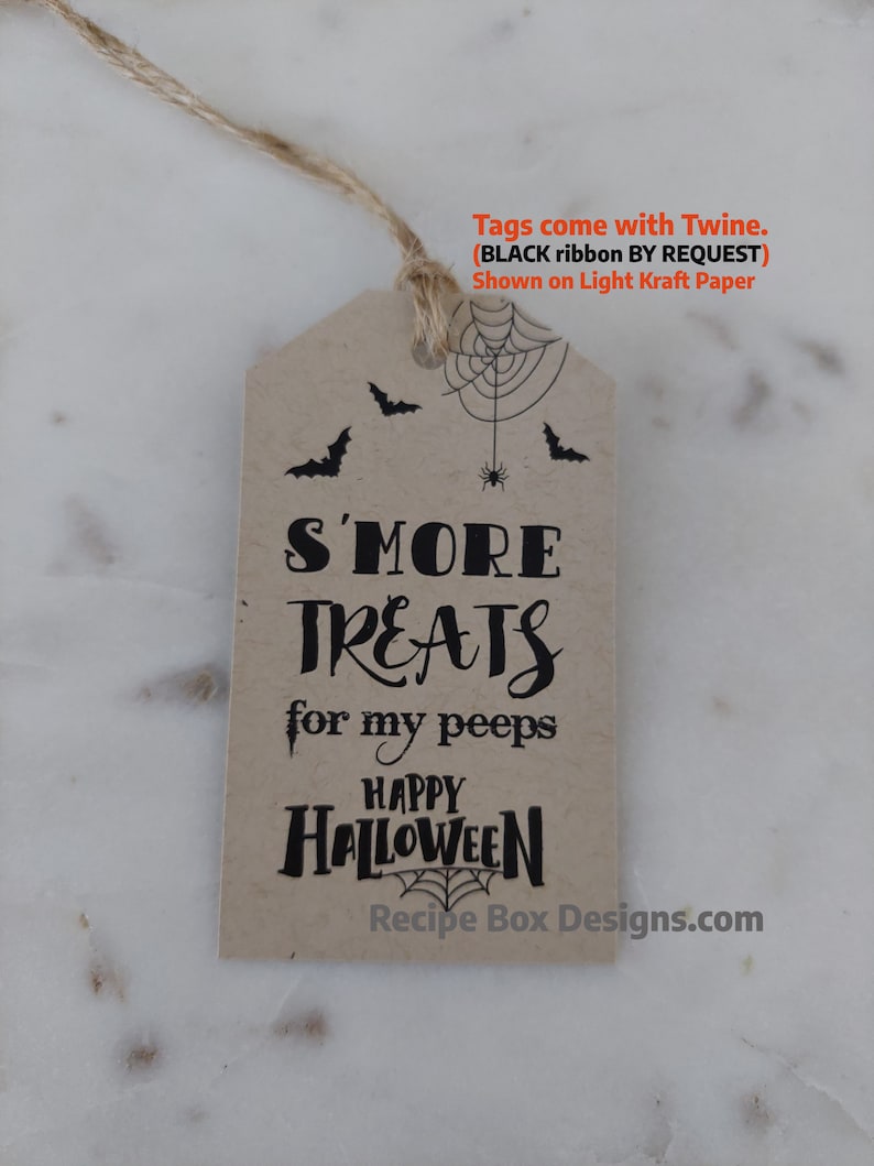 May include: A light kraft paper tag with a twine string. The tag features black text that reads "S'MORE TREATS for my peeps HAPPY HALLOWEEN." A spider web and bats are also printed on the tag. The text "Recipe Box Designs.com" is at the bottom.