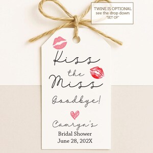 May include: A white tag with the text "Kiss the Miss Goodbye!" and "Camryn's Bridal Shower June 28, 202X". The tag features pink lip prints and a heart, tied with twine.