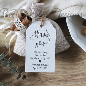 May include: White thank you tag with black calligraphy that reads "thank you" and the text "for traveling near or far by plane or by car! Jennifer & Gage April 15, 2023".