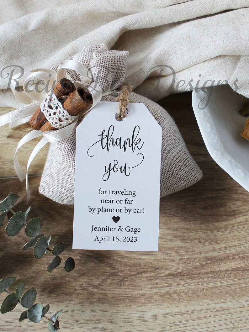 May include: White thank you tag with black calligraphy that reads "thank you" and the text "for traveling near or far by plane or by car! Jennifer & Gage April 15, 2023".