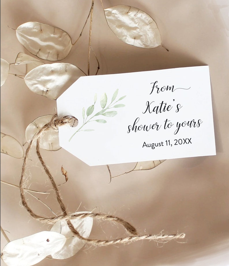 May include: A white gift tag with a green leafy branch design. The tag has the text "from Katie's shower to yours" and "August 11, 20XX". The tag is tied with a brown twine string.