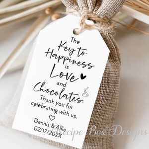 Puede incluir: Una etiqueta blanca con texto negro que dice "The Key to Happiness is Love and Chocolates." La etiqueta est&aacute; atada a una peque&ntilde;a bolsa de arpillera. El texto tambi&eacute;n incluye "Thank you for celebrating with us." y "Dennis & Allie 02/17/202X".