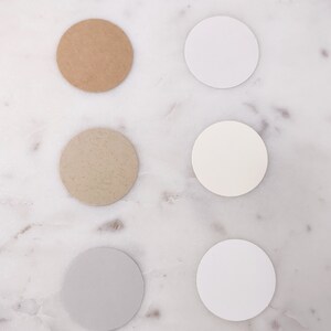 May include: Six round paper samples in different shades of white, beige, and brown. The samples are arranged in two vertical rows of three.