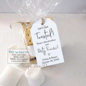 May include: A clear cellophane bag tied with twine, containing a graham cracker and marshmallow s'more. A white tag with the text "Let's Get Toasted!" is attached. The tag also includes the names Ashley & Robert and the date October 26, 20XX.