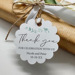 May include: A white scalloped gift tag with the words "Thank you" in elegant script, accented with watercolor eucalyptus leaves. The tag is tied to a wrapped gift with twine and a white ribbon.