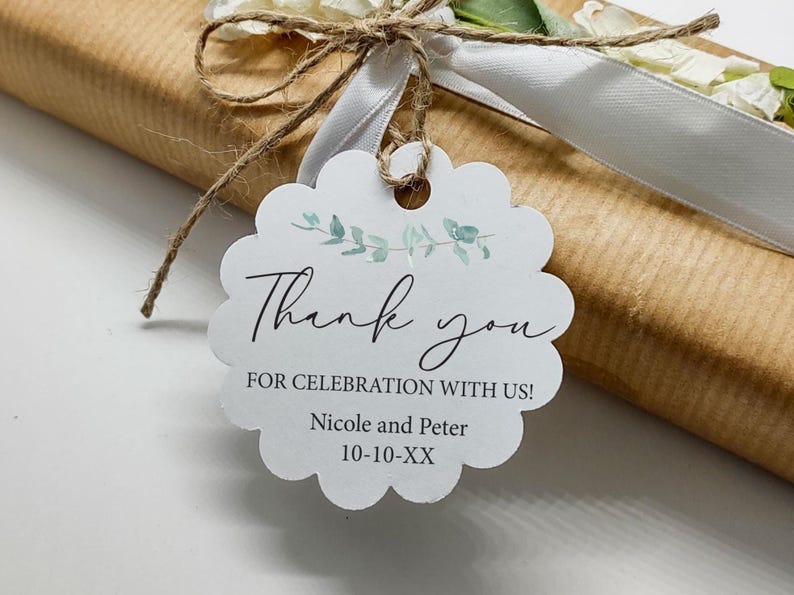 May include: A white scalloped gift tag with the words "Thank you" in elegant script, accented with watercolor eucalyptus leaves. The tag is tied to a wrapped gift with twine and a white ribbon.