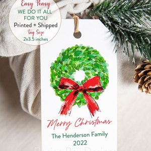 May include: A white Christmas gift tag with a watercolor wreath and red bow design. The tag reads "Merry Christmas," the family name, and the year 2022. Tag size is 2x3.5 inches.