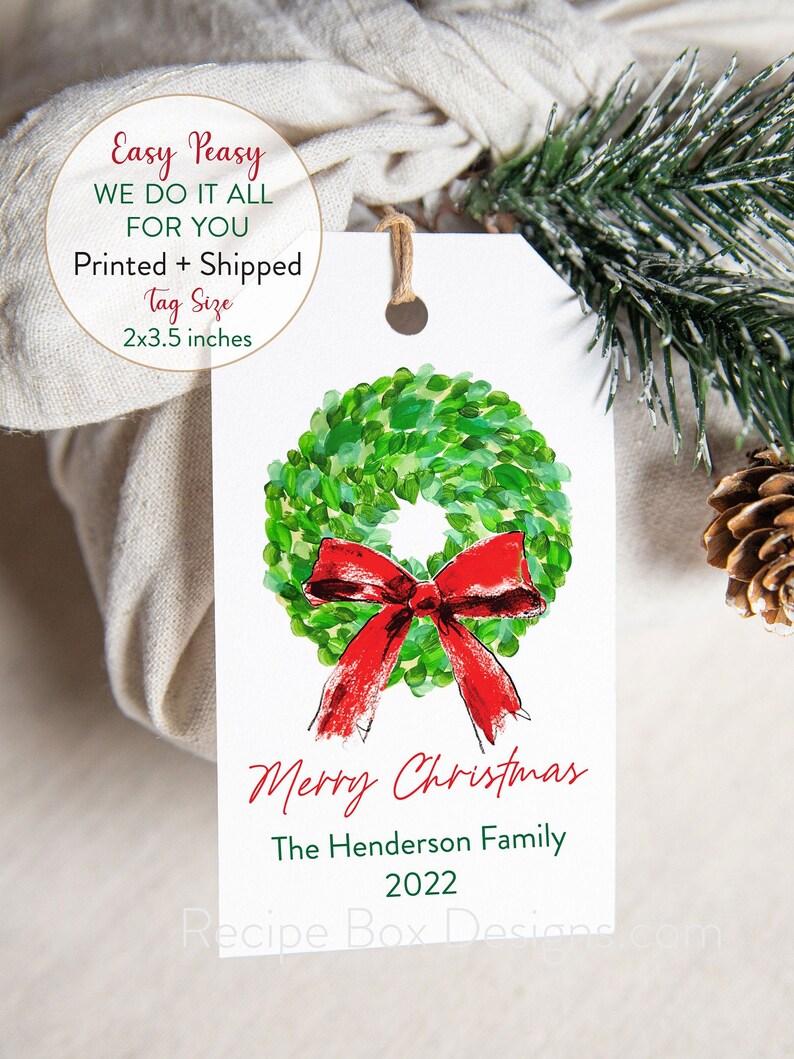 May include: A white Christmas gift tag with a watercolor wreath and red bow design. The tag reads "Merry Christmas," the family name, and the year 2022. Tag size is 2x3.5 inches.
