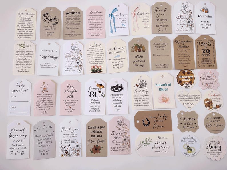 May include: A collection of assorted gift tags and labels in various shapes and sizes. The tags feature printed text, floral designs, and decorative elements. Some tags include phrases like "Thank You," "Happy Birthday," and "Welcome."