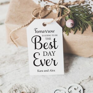 K&ouml;nnte beinhalten: Wei&szlig;er Geschenkanh&auml;nger mit schwarzem Text, der "Morgen wird der beste Tag aller Zeiten" und "Kara und Alex" lautet.