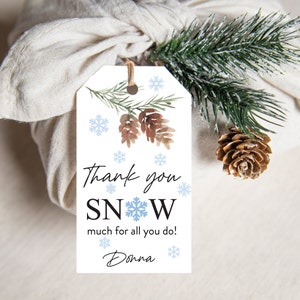 May include: A white gift tag with the text "Thank you SNOW much for all you do!" and the name "Donna". The tag features watercolor pinecones, snowflakes, and a sprig of evergreen. The tag is tied with twine.