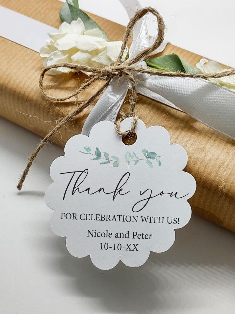 May include: A gift wrapped in brown paper, tied with white ribbon and twine, and adorned with a white flower. A scalloped tag reads "Thank you" with the names Nicole and Peter and a date.