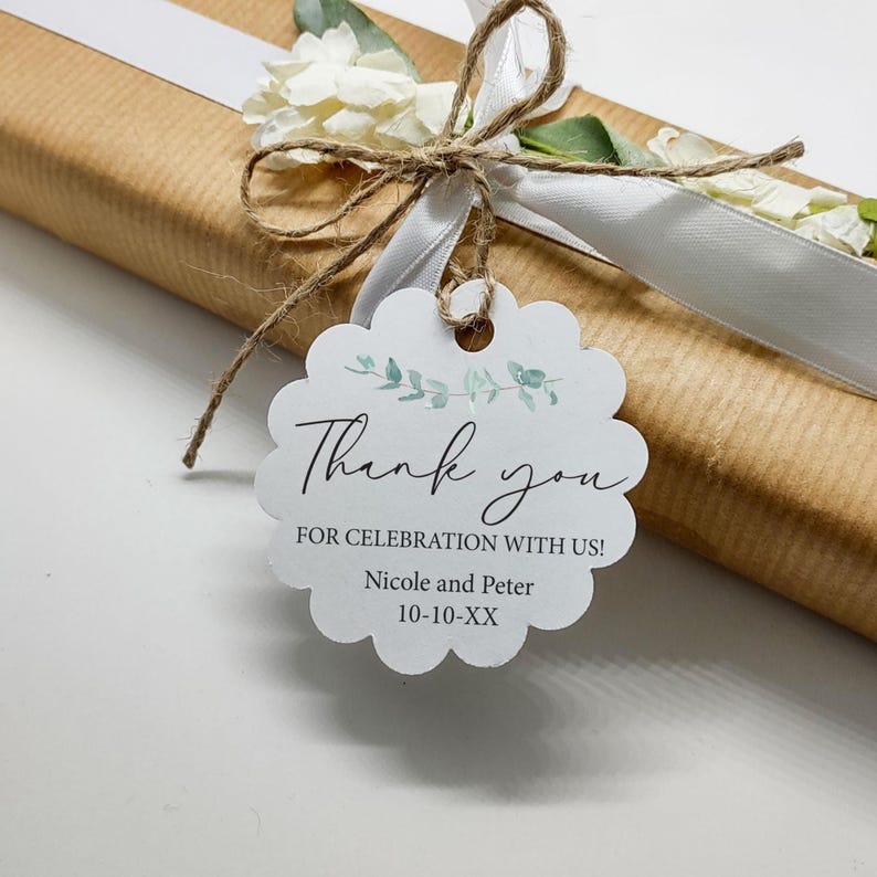 May include: A wrapped gift in brown paper, tied with a white ribbon and twine. A white scalloped tag with the words "Thank you" and "For Celebration With Us!" is attached. The tag also includes the names "Nicole and Peter" and the date "10-10-XX".