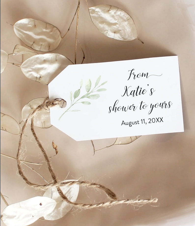 May include: A white gift tag with a green leafy branch design. The tag has the text "from Katie's shower to yours" and "August 11, 20XX". The tag is tied with a brown twine string.