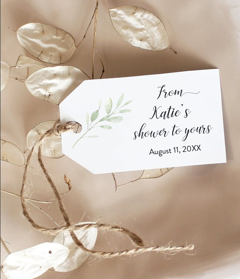 May include: A white gift tag with a green leafy branch design. The tag has the text "from Katie's shower to yours" and "August 11, 20XX". The tag is tied with a brown twine string.