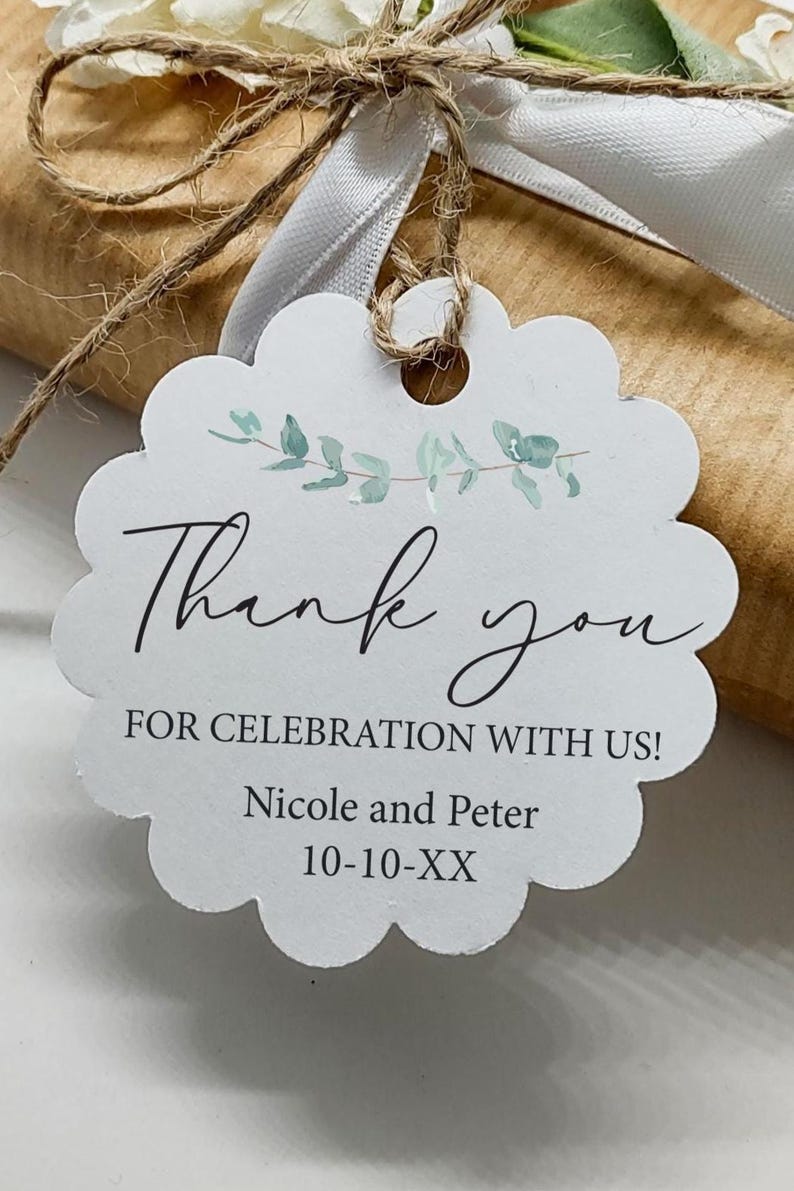 May include: A white scalloped-edge gift tag with the words "Thank you" in elegant script. The tag includes the text "FOR CELEBRATION WITH US!" and the names "Nicole and Peter" with a date. The tag is tied with twine and a white ribbon.