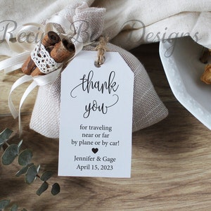 May include: A white thank you tag with a burlap bag filled with cinnamon sticks. The tag says "thank you" in cursive and "for traveling near or far by plane or by car! Jennifer & Gage April 15, 2023".