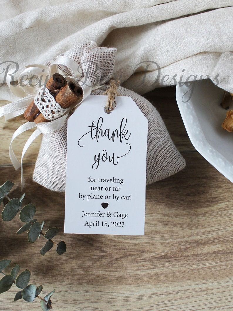 May include: A white thank you tag with a burlap bag filled with cinnamon sticks. The tag says "thank you" in cursive and "for traveling near or far by plane or by car! Jennifer & Gage April 15, 2023".