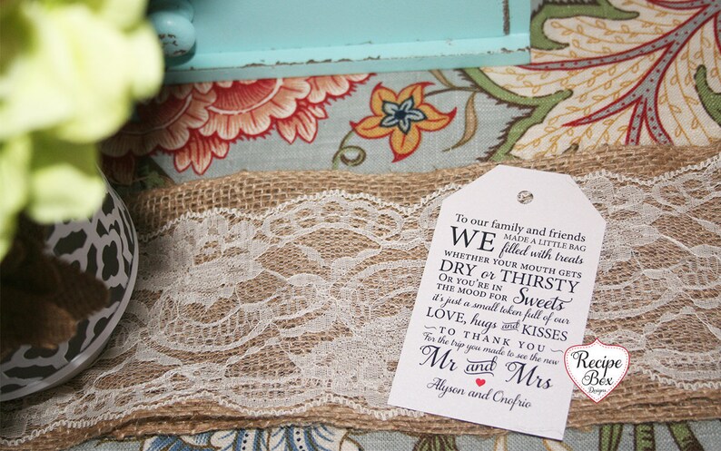 May include: A white gift tag with black text that reads "To our family and friends WE made a little bag filled with treats WHETHER YOUR MOUTH GETS DRY or THIRSTY OR YOU'RE IN THE MOOD FOR Sweets it's just a small token full of our LOVE, hugs KISSES TO THANK YOU for the trip you made to see the new Mr and Mrs Alyson and Onofrio". The tag is sitting on a burlap surface with white lace.