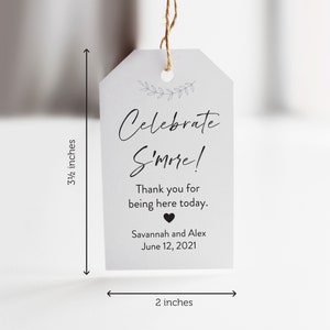 May include: A white tag with black text that reads "Celebrate S'more!"  Thank you for being here today. Savannah and Alex June 12, 2021. The tag is 3 1/2 inches tall and 2 inches wide.