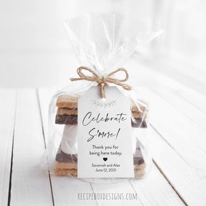 May include: A white gift tag with black text that reads "Celebrate S'more!"  Thank you for being here today. Savannah and Alex June 12, 2021. The tag is tied to a clear cellophane bag filled with graham crackers, chocolate, and marshmallows.