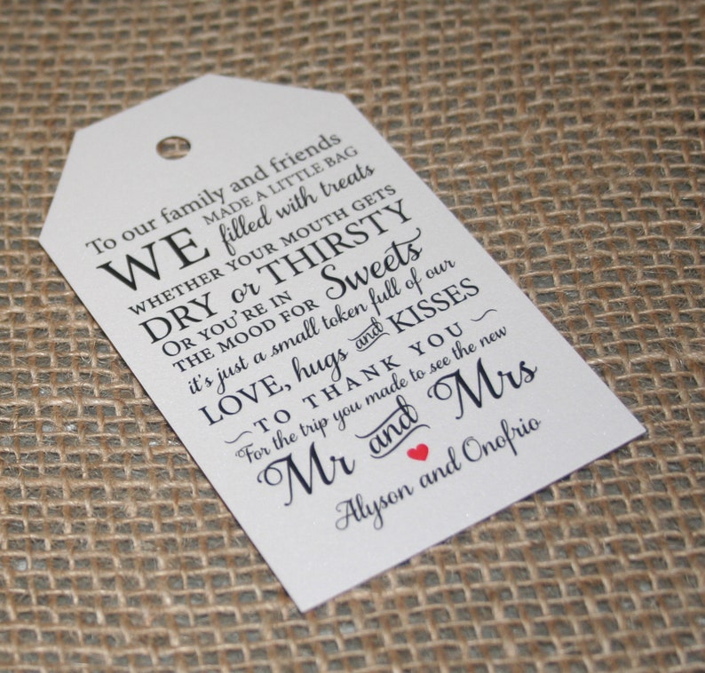 May include: White wedding favor tag with black text that reads "To our family and friends WE made a little bag filled with treats WHETHER YOUR MOUTH GETS DRY or THIRSTY OR YOU'RE IN THE MOOD FOR Sweets it's just a small token full of our LOVE, hugs and KISSES TO THANK YOU~ For the trip you made to see the new Mr and Mrs Alyson and Onofrio".